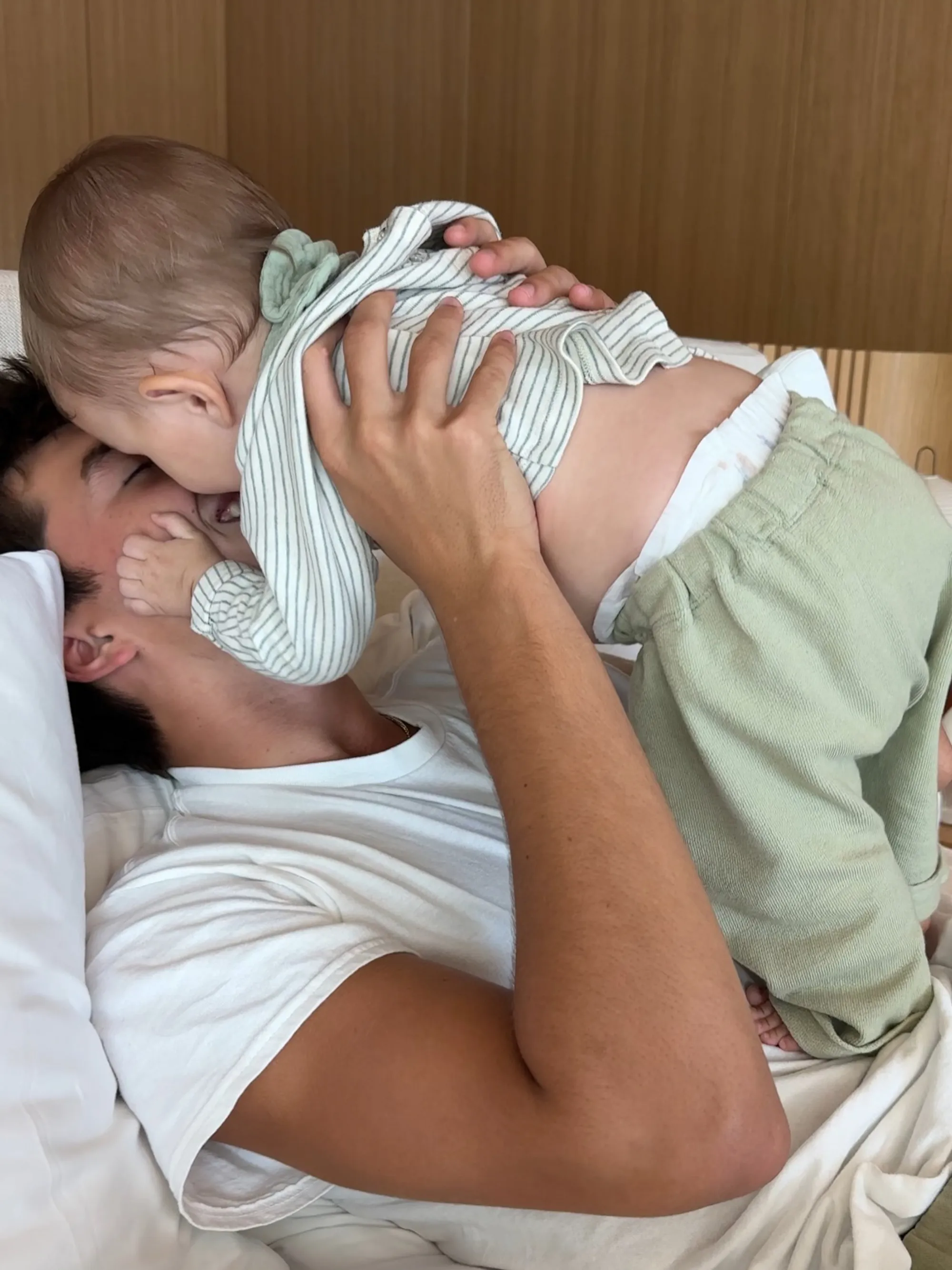 Person lying on their back holding a baby, whose face is obscured, above their chest.