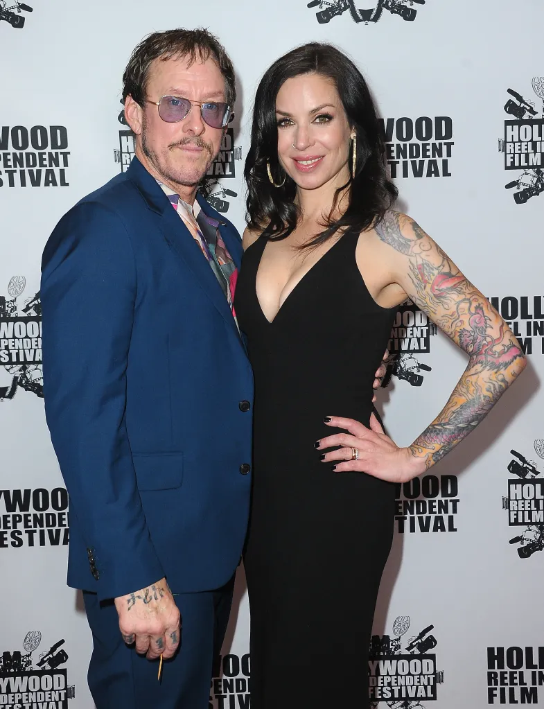 Scott Shriner and Jillian Lauren pose together on a white step-and-repeat banner.