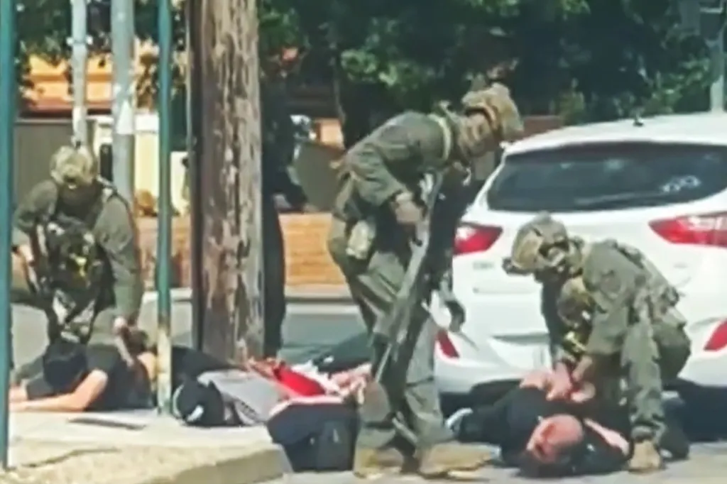 Heavily armed police officers arresting men on the ground.