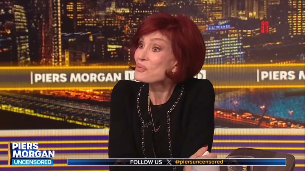 Sharon Osbourne with reddish-brown hair sitting in front of a city lights backdrop on Piers Morgan Uncensored.