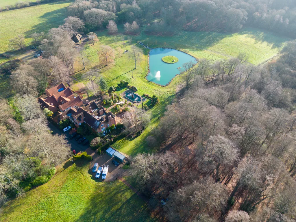 Aerial view of Sharon Osbourne's home in Buckinghamshire with a large house, a small pond, and surrounding trees and fields.