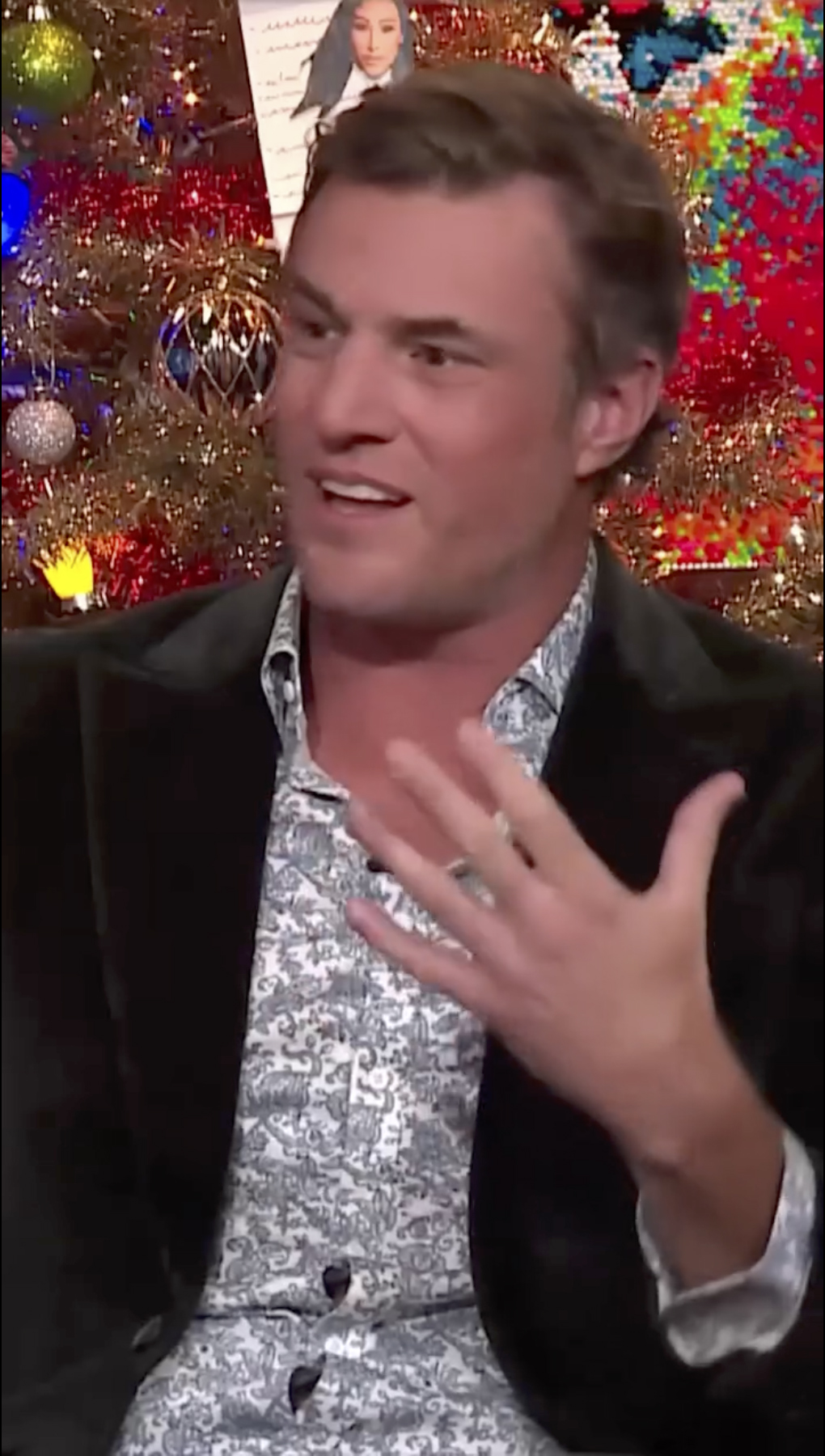 Shep Rose gestures while wearing a patterned shirt and dark jacket.
