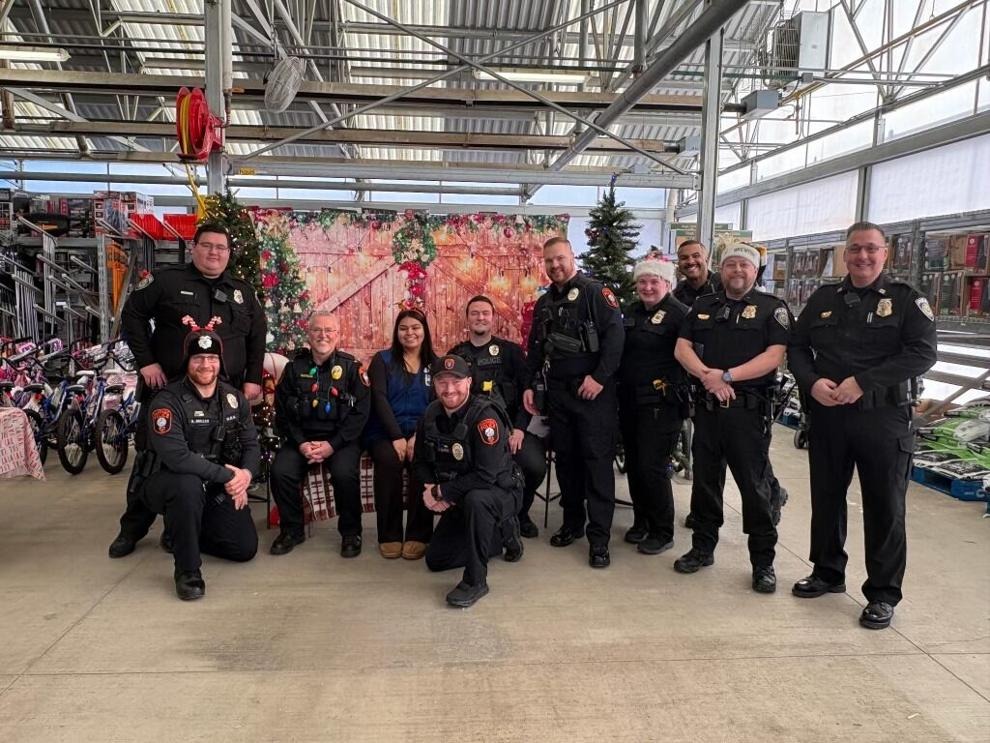 Police officers and a woman pose in front of a holiday backdrop at a Shop with a Cop event.