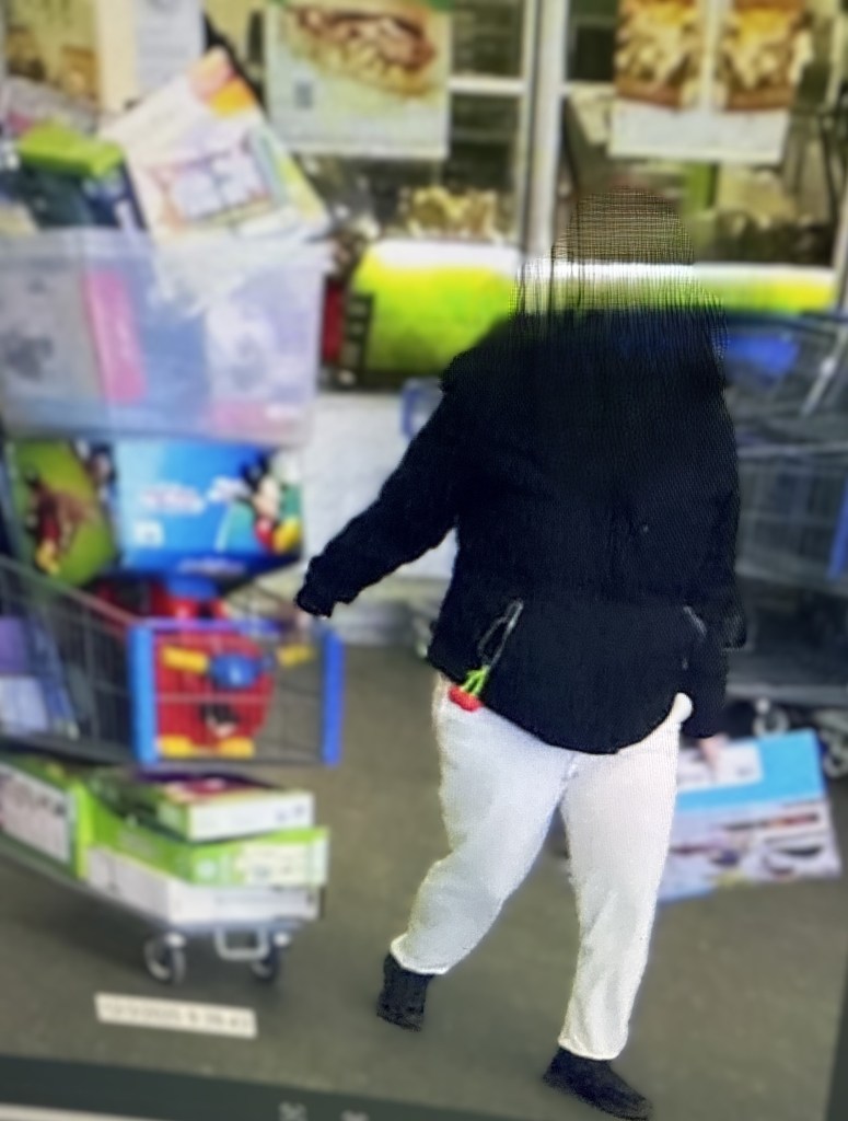 A shoplifter with a blurred face walks past a shopping cart filled with items.