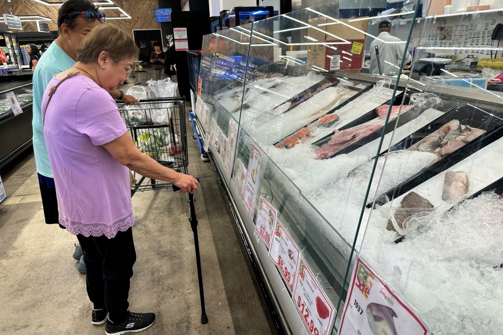 Shoppers checking prices at the fish department in a grocery store.