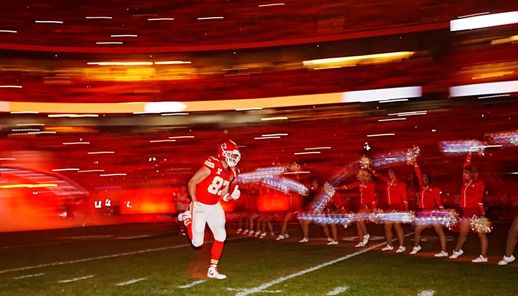 Kansas City Chiefs player Travis Kelce running past cheerleaders on the field.