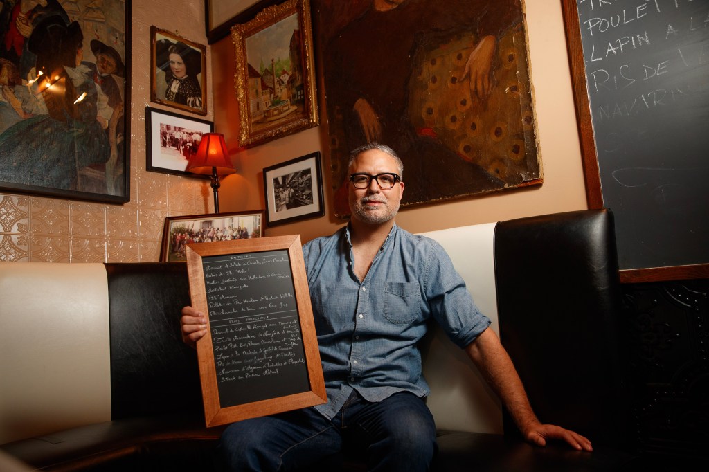 Karim Raoul, owner of Raoul's, holding a chalkboard menu of entrees and main dishes.