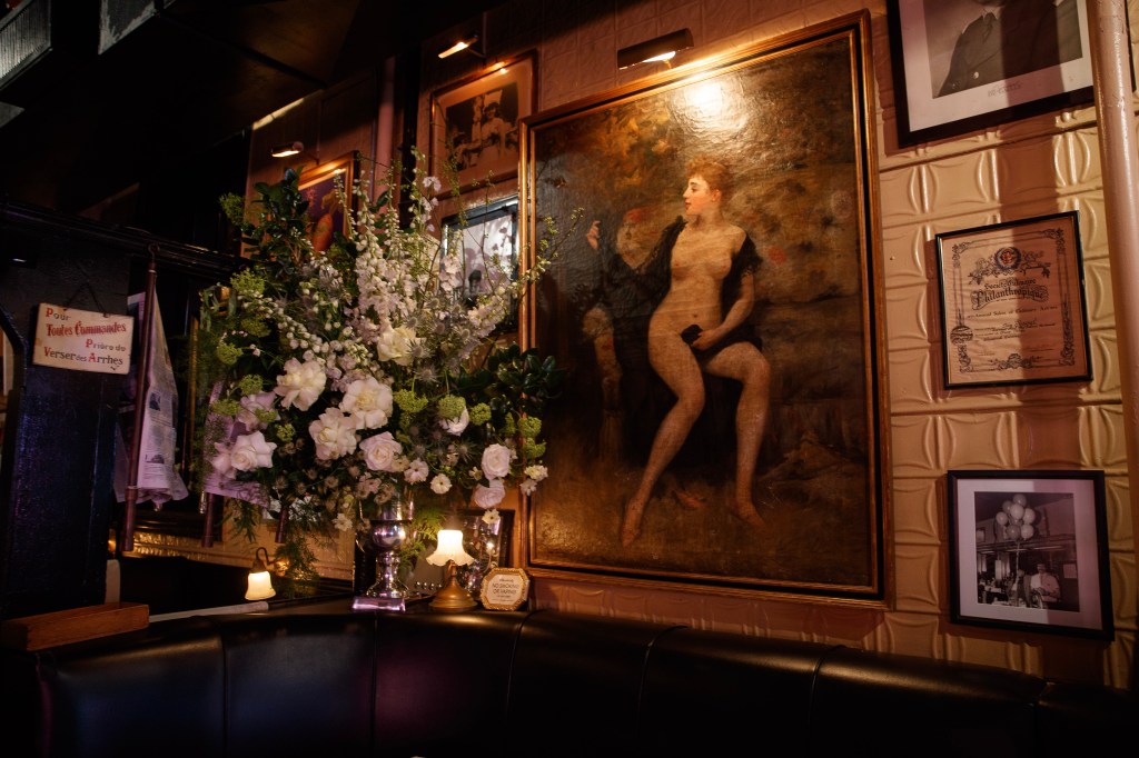 Interior of Raoul's restaurant with a large painting of a reclining nude woman, floral arrangements, and framed photos and awards on the wall.