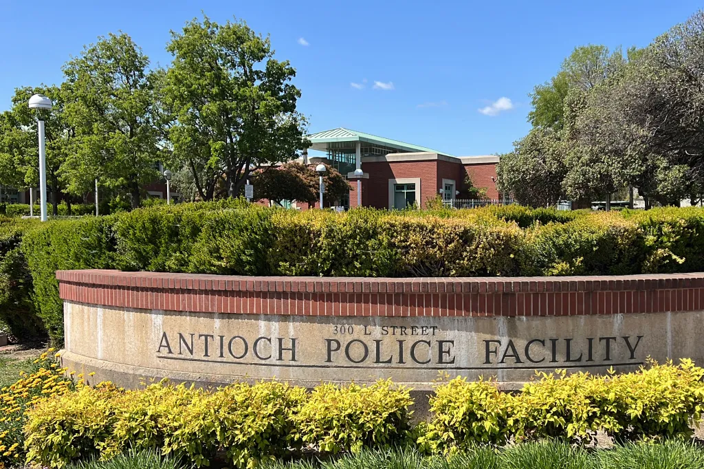 A sign for the Antioch Police Facility, with the building visible behind hedges and trees.
