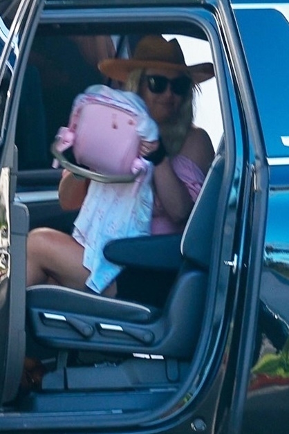 Britney Spears exiting a car, wearing a wide-brim hat and sunglasses, carrying a pink baby carrier.