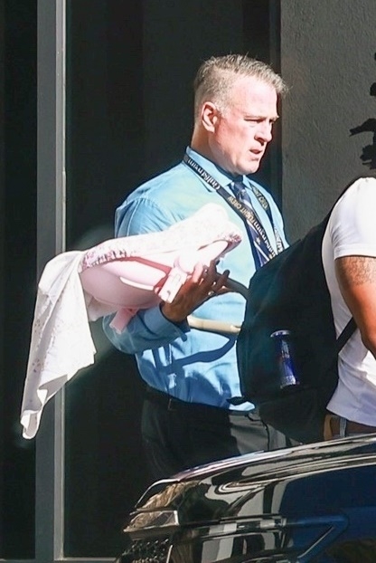 Security guard carrying a pink baby carrier with a white blanket.