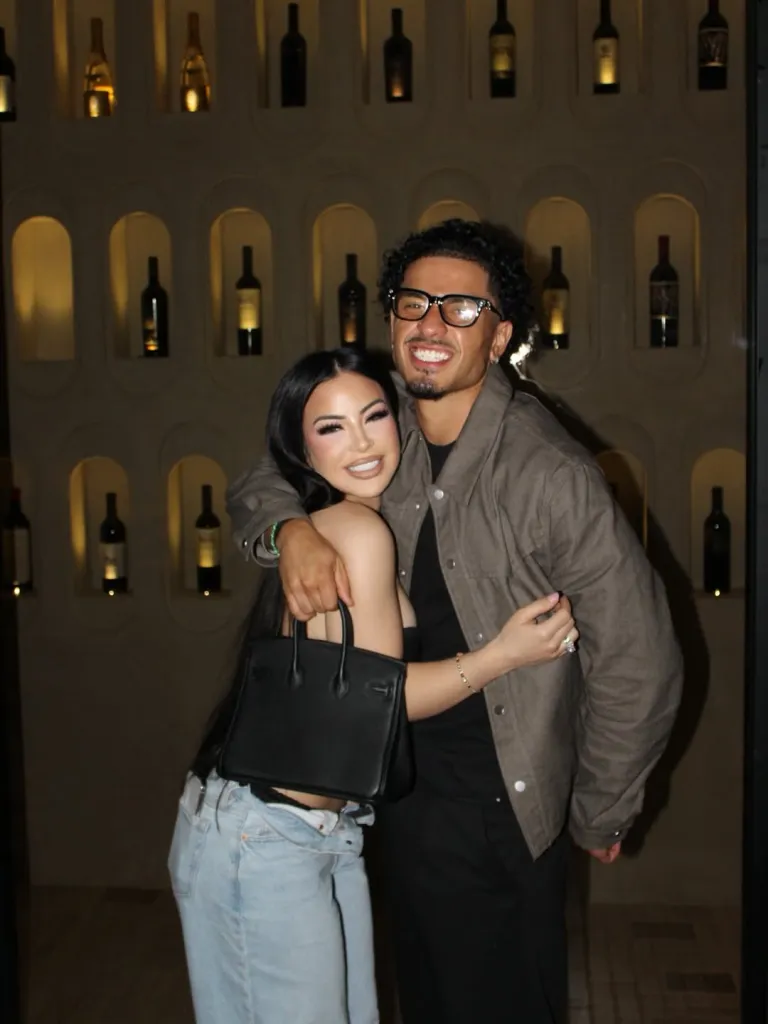 A man in glasses with a beard and a woman with dark hair smile, with their arms around each other.