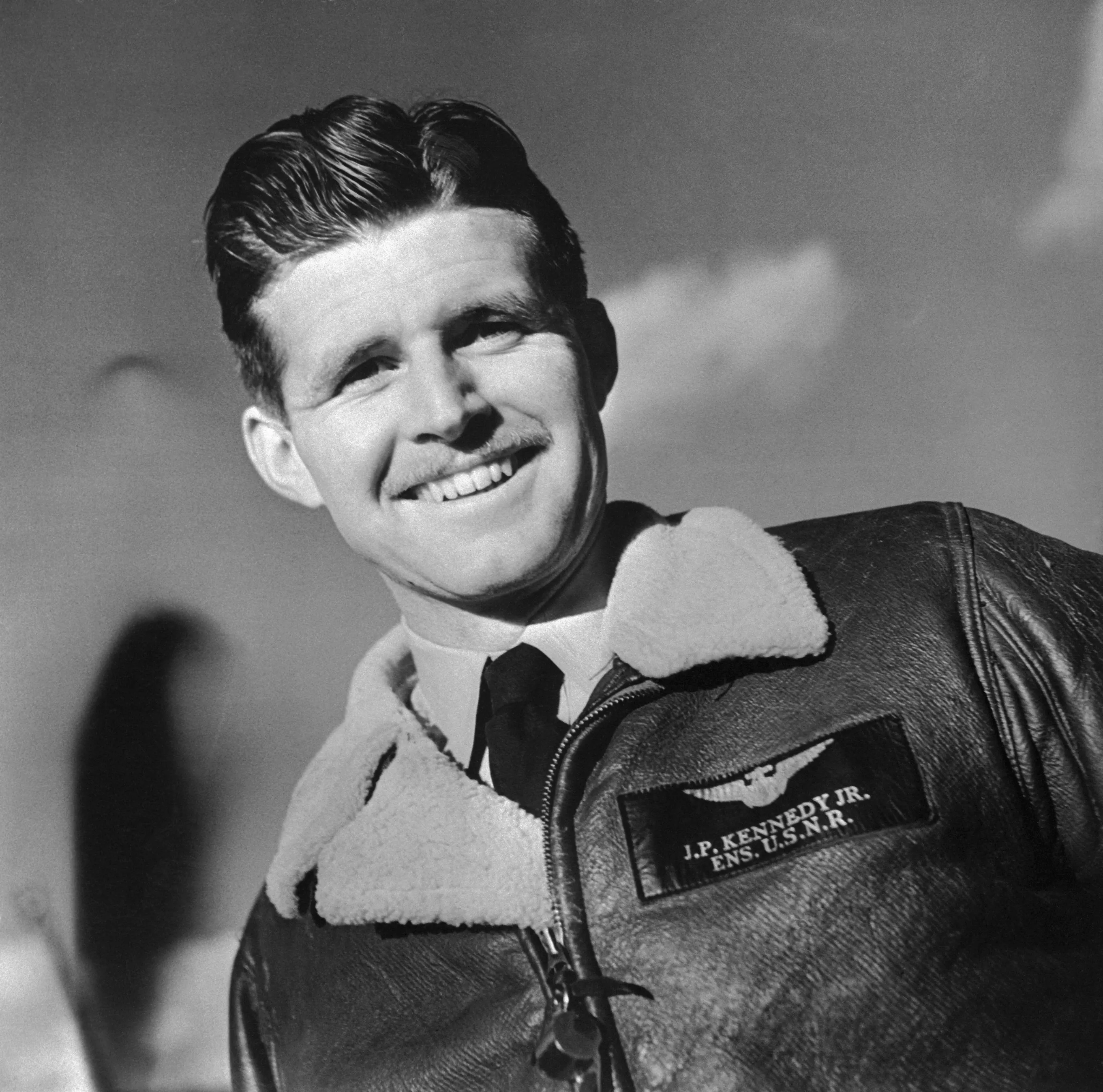 Portrait of Lieutenant Joseph P. Kennedy Jr. smiling in a leather flight jacket.
