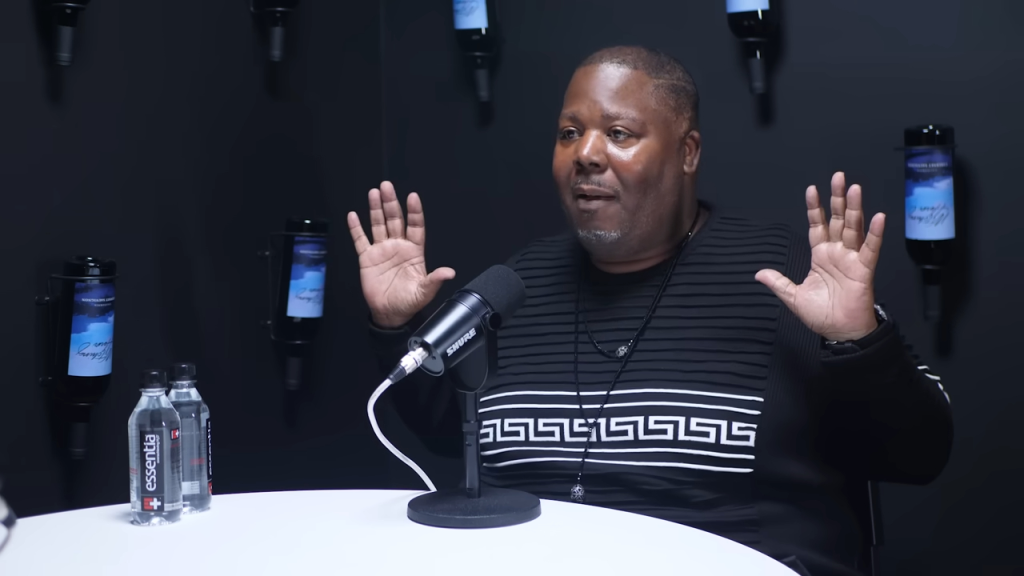 A man speaking into a Shure microphone with his hands raised.