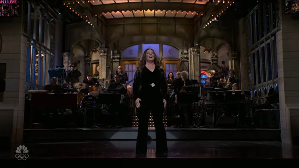 Melissa McCarthy performing on the SNL stage with the band behind her.