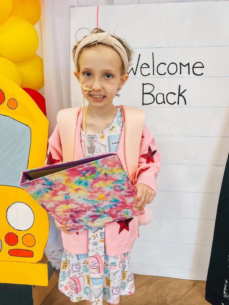 Brie Bird holds a binder as she poses in front of a welcome sign.