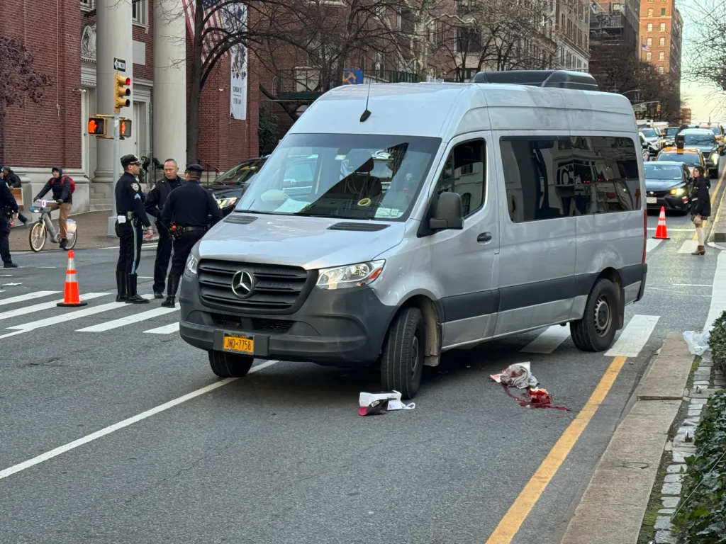A grey van stopped in the street with a pool of blood next to it.