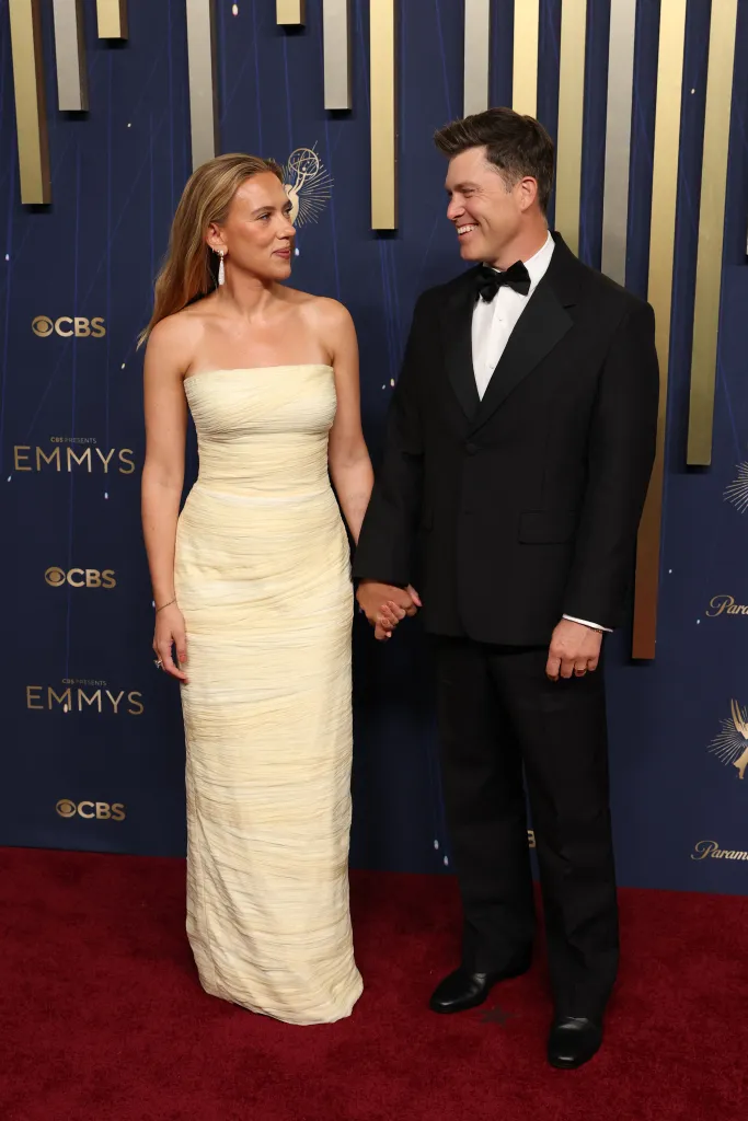 Scarlett Johansson in a light yellow strapless gown and Colin Jost in a black tuxedo on the red carpet.