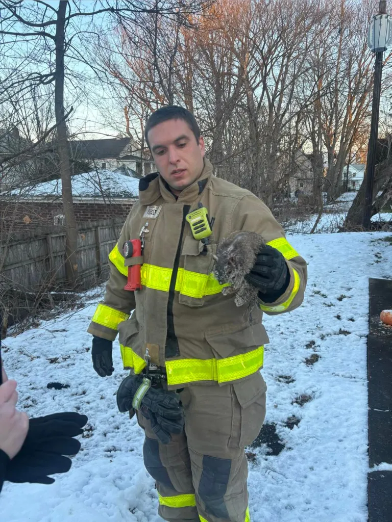 A firefighter in winter gear holding a small, wet squirrel.