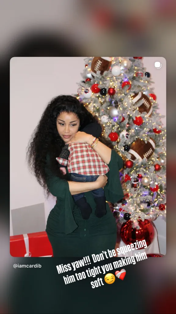 Cardi B holding a baby in front of a Christmas tree decorated with footballs.
