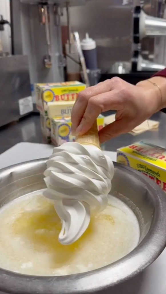 A hand dipping a vanilla soft-serve ice cream cone into a bowl of melted Stew Leonard's-brand butter.