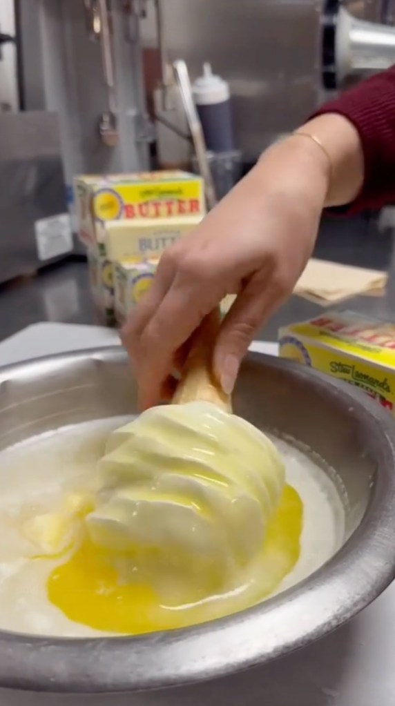 A hand dipping a vanilla soft-serve cone into a bowl of melted Stew Leonard's brand butter.