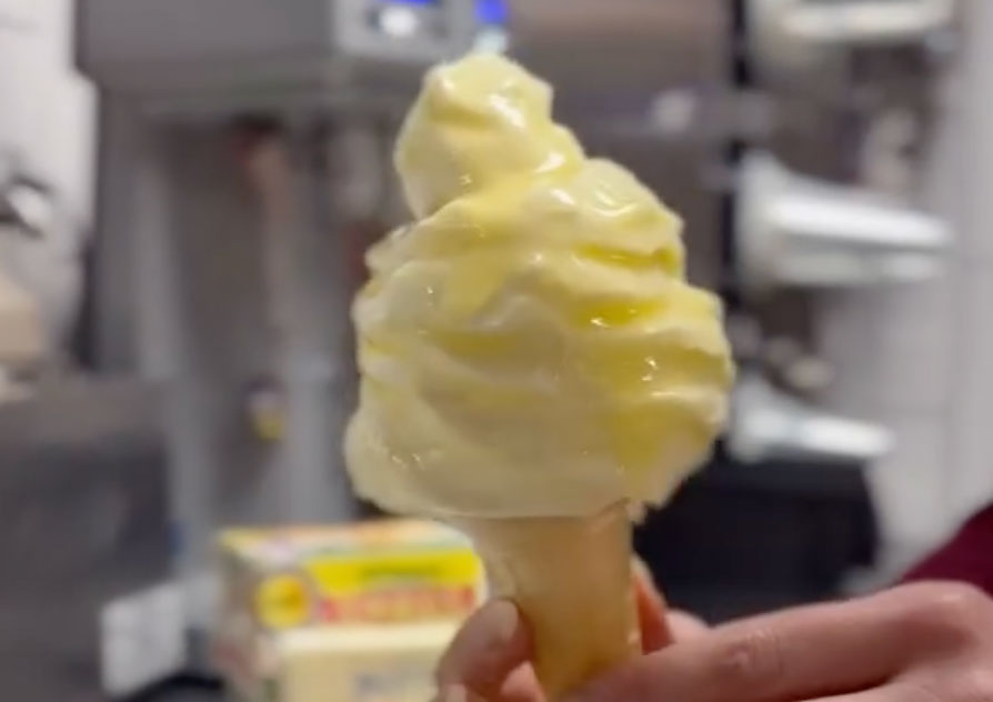 A vanilla soft-serve ice cream cone being dipped in melted butter.