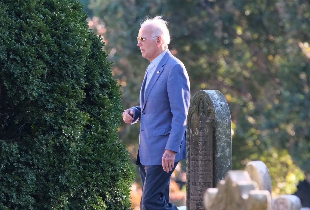 Joe Biden walking past a bush and tombstones in a cemetery.