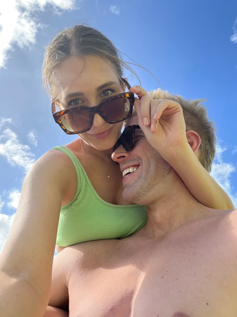 Amanda Batula wearing sunglasses on her head and Kyle Cooke laughing with sunglasses on his face, under a blue sky.