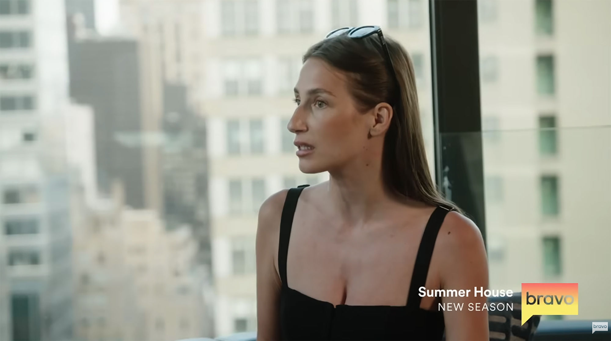 Amanda Batula of Summer House in a black top with sunglasses on her head, looking away.
