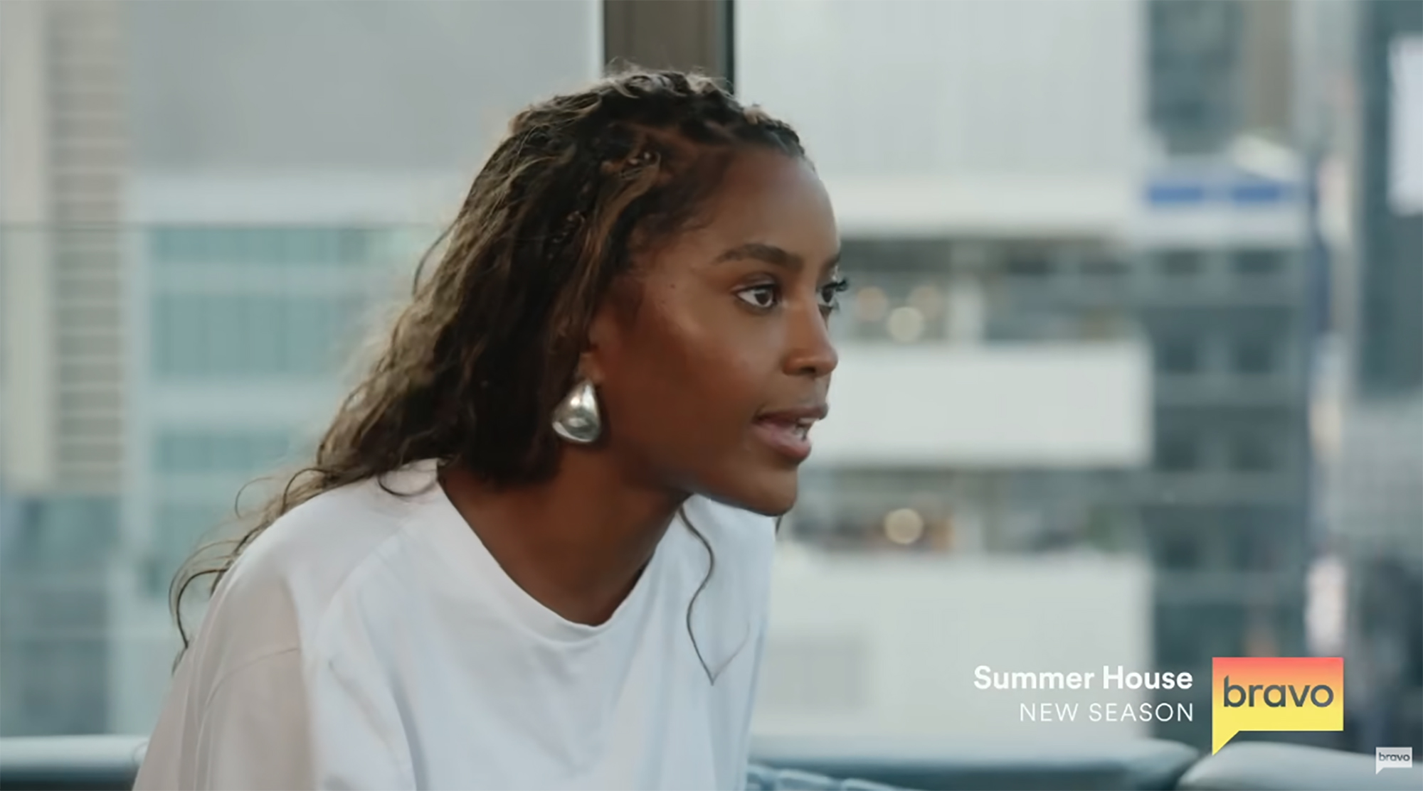 A woman with braided hair and silver earrings looks to the right, talking.