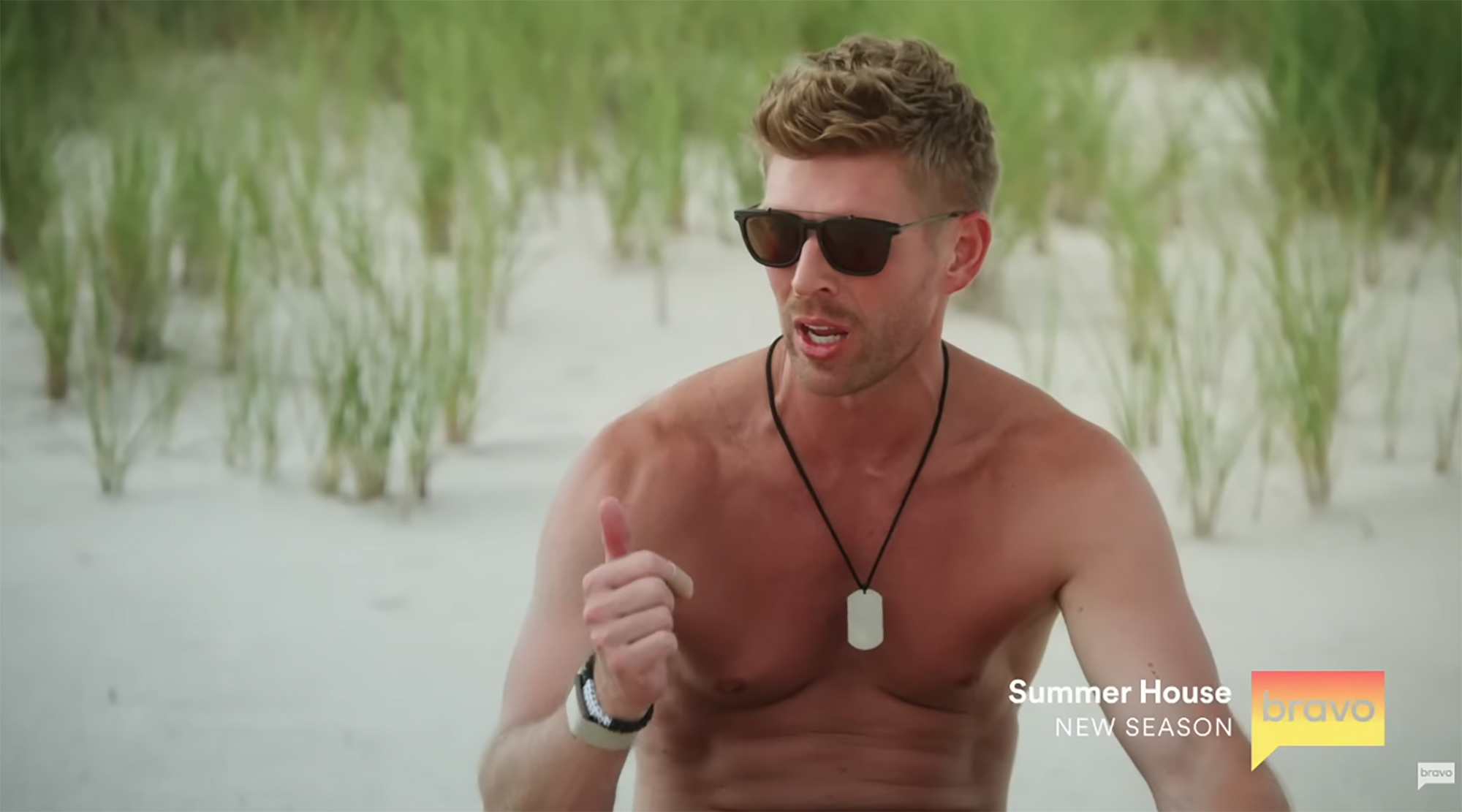 Kyle Cooke, wearing sunglasses and no shirt, makes a point with a hand gesture.