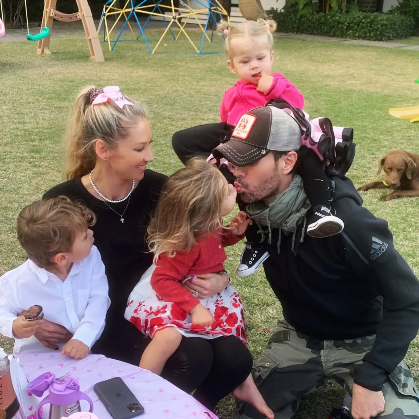 Enrique Iglesias and Anna Kournikova with their three children and a dog in a backyard.