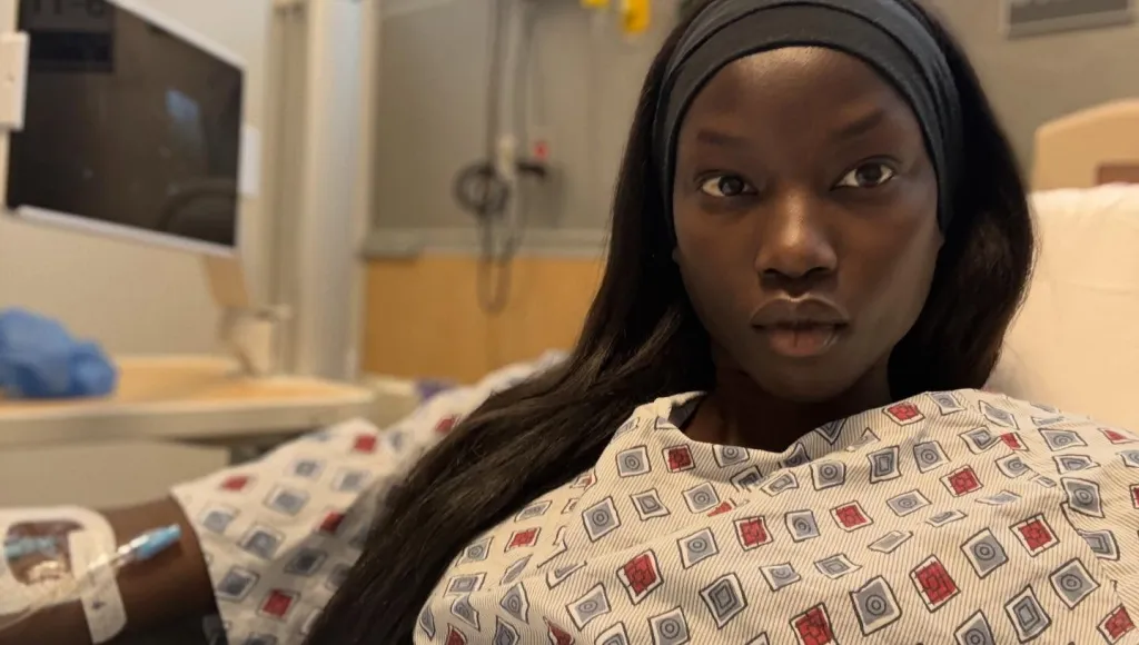 Supermodel Anok Yai in a hospital bed with an IV drip in her arm.