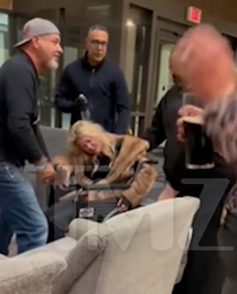 Tara Reid unconscious in a wheelchair in a hotel lobby surrounded by several men.
