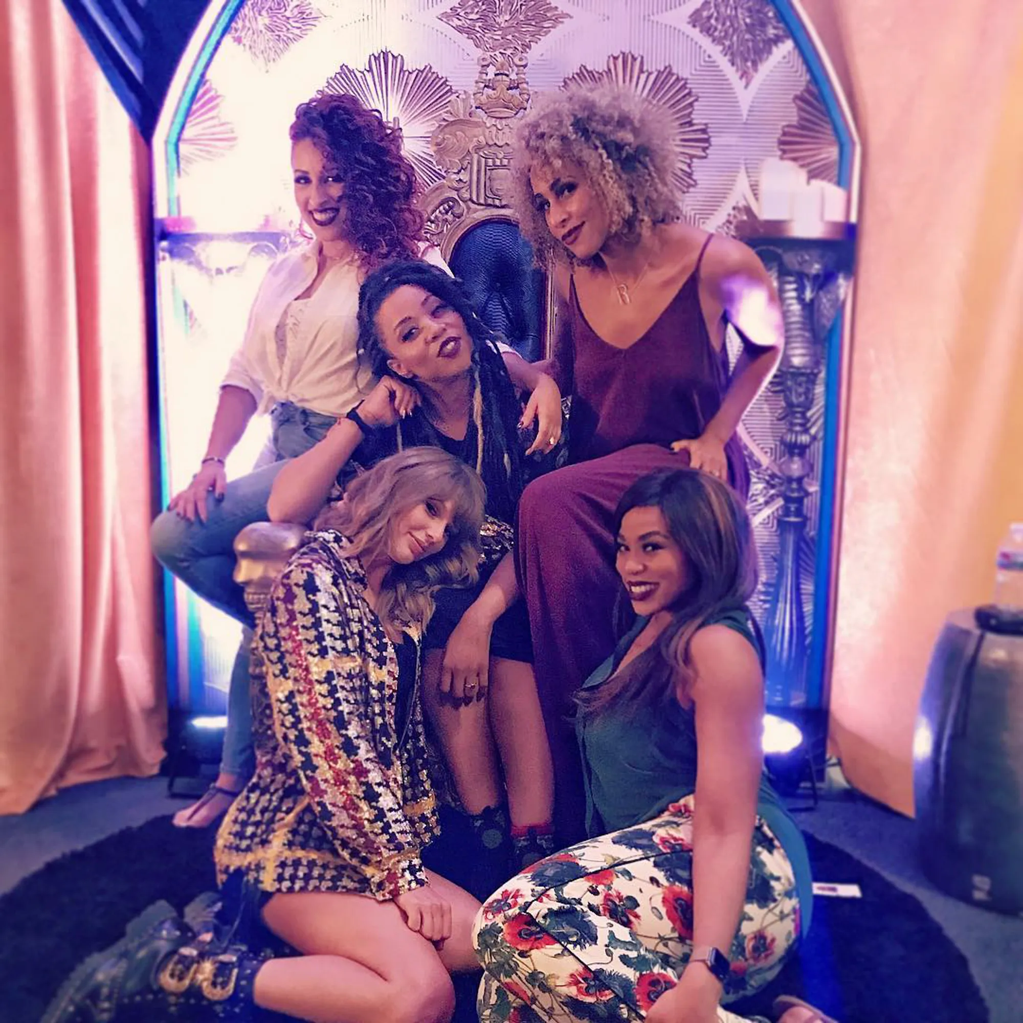 Taylor Swift and four women dancers pose around a gold chair in a decorated room.