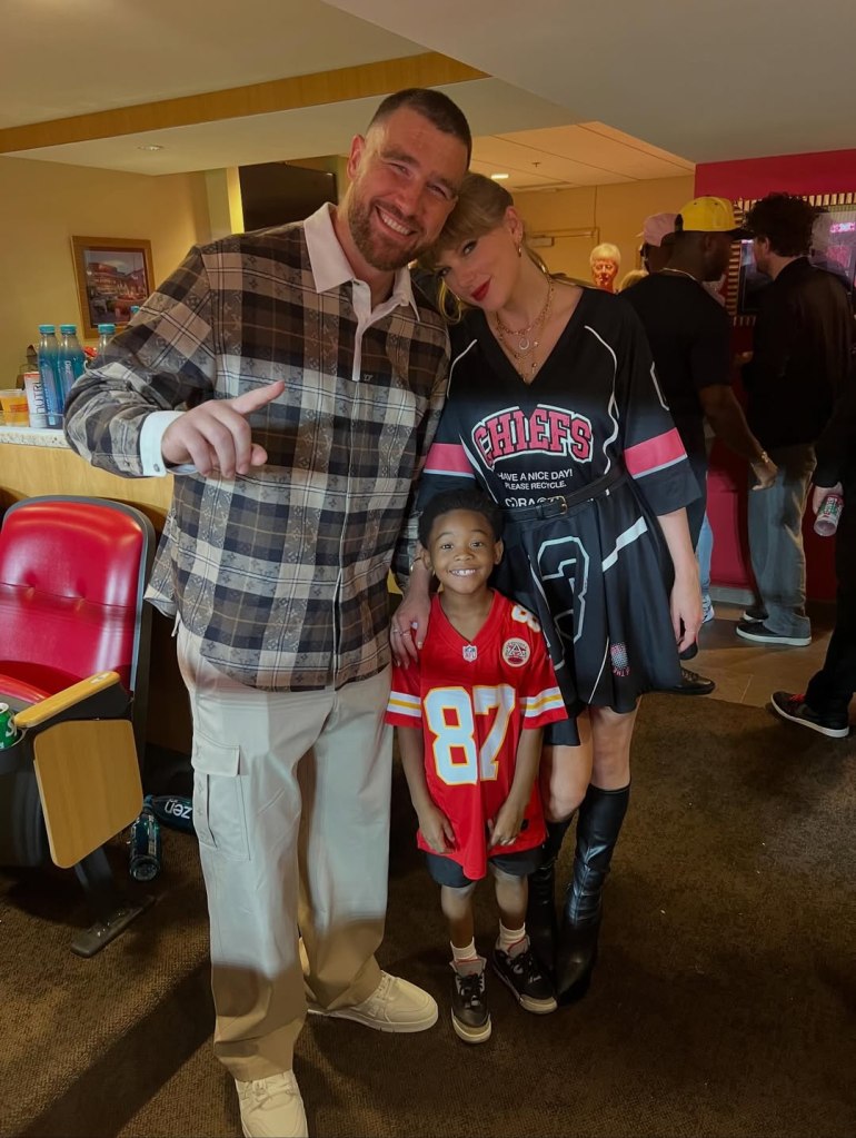 Travis Kelce, Taylor Swift, and a child wearing a Chiefs jersey pose for a photo.