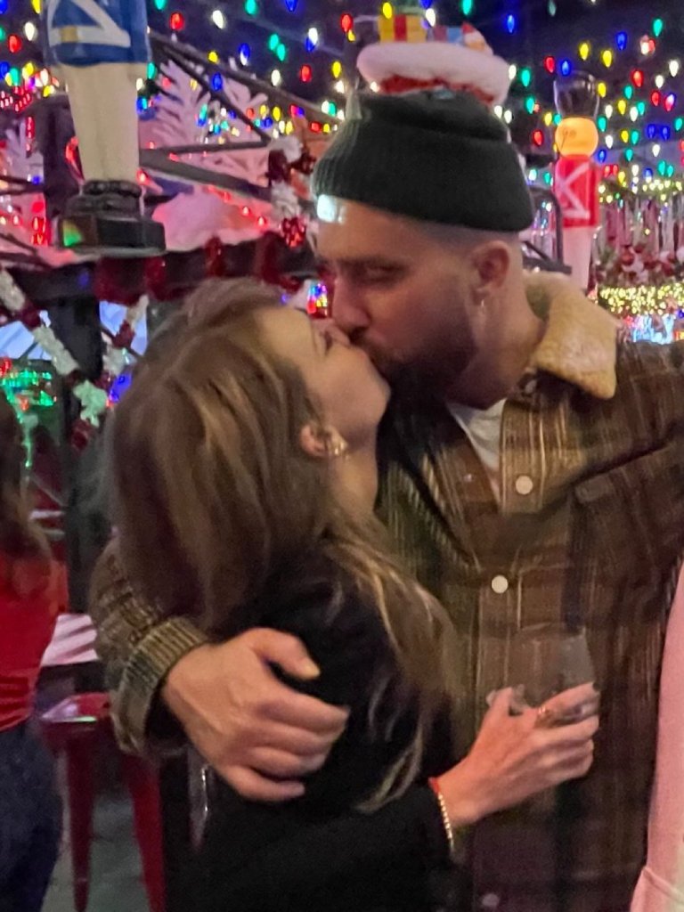 Taylor Swift and Travis Kelce kissing against a background of colorful string lights.