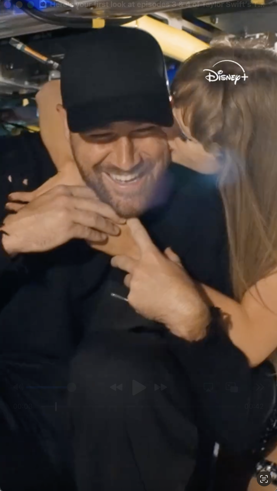 Taylor Swift embraces Travis Kelce from behind, who is smiling broadly, with the Disney+ logo visible.