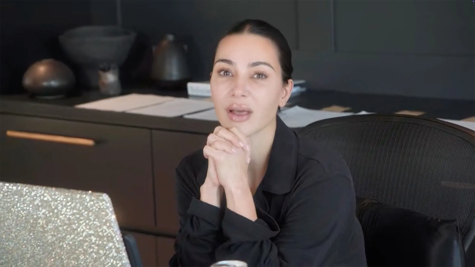 A tearful Kim Kardashian with clasped hands looking forward.