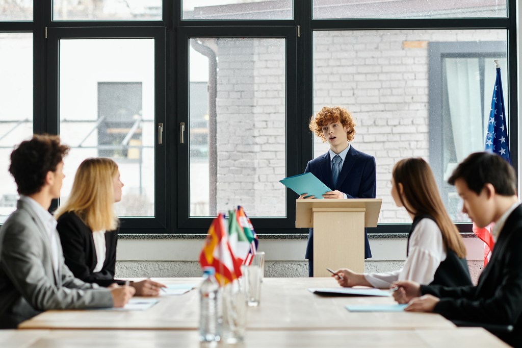Teenagers listen attentively at a Model UN conference as a peer gives a speech.