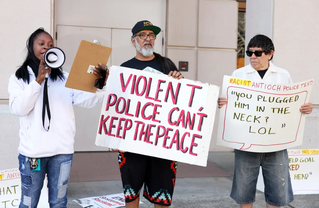 Protesters Teki Flow, Frank Sterling, and Francisco Torres hold signs in front of a courthouse against police violence and racism.