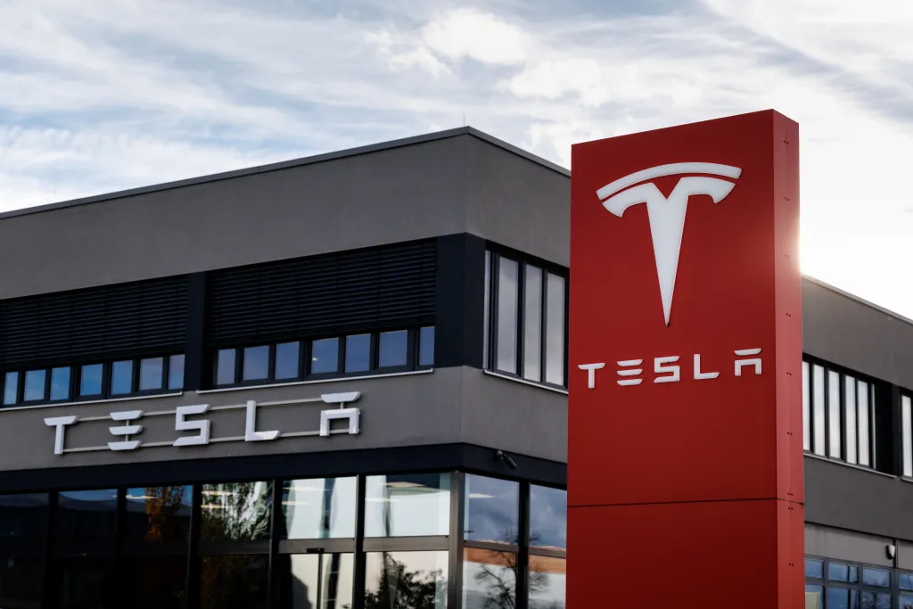 Tesla logo on a red sign in front of a dark building with the Tesla name.