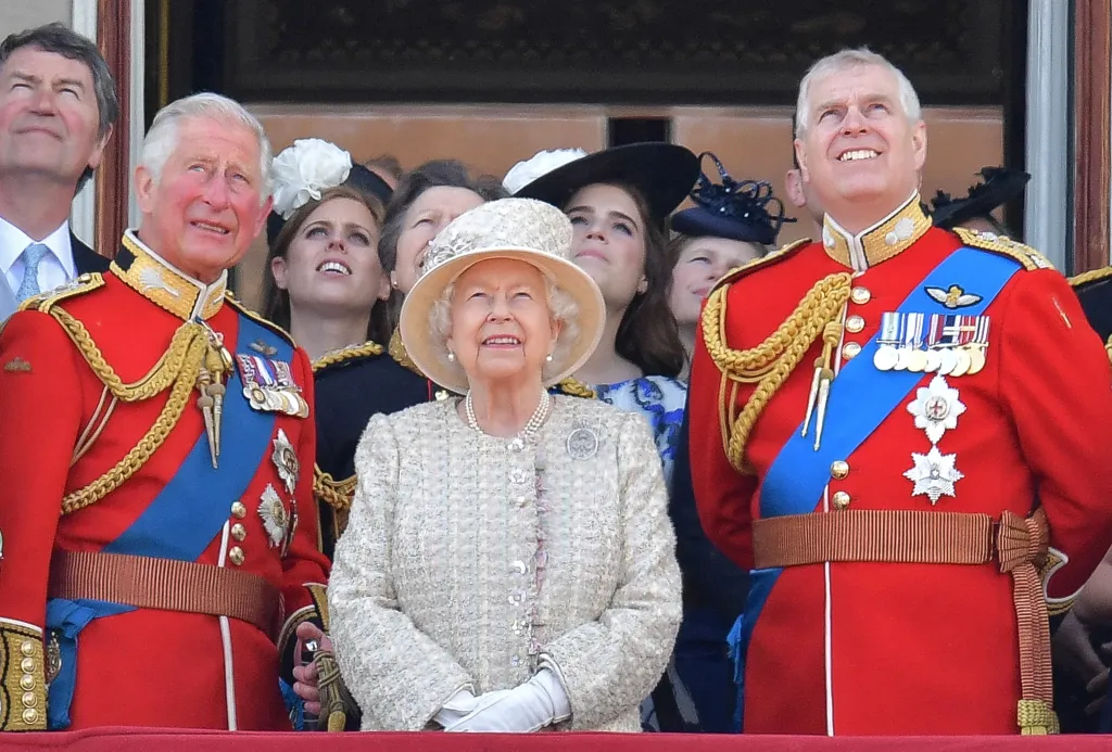 Queen Elizabeth II stands on the balcony of Buckingham Palace, surrounded by other members of the Royal Family, watching a fly-past.