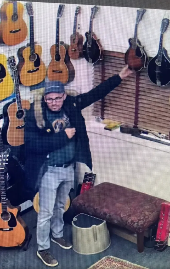 A man in a cap and coat holding a mandolin in a music store.