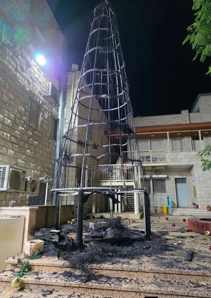 A burned Christmas tree frame with charred debris and scattered ornaments in front of a building.