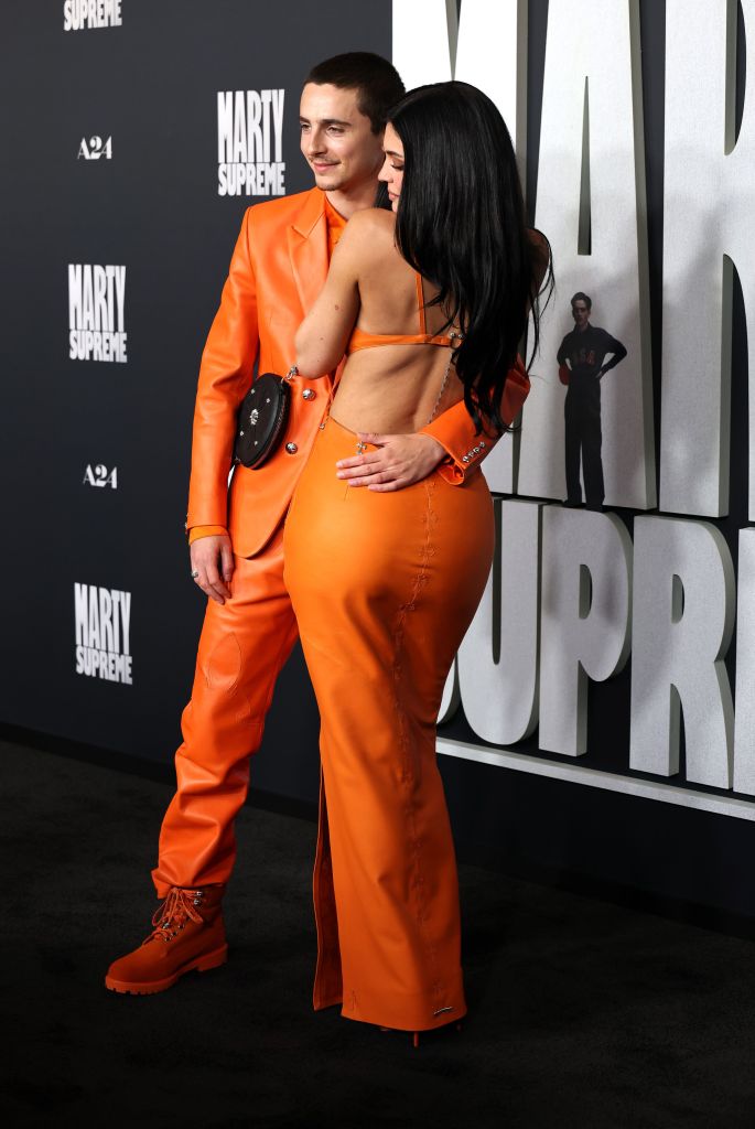 Timothée Chalamet and Kylie Jenner pose in orange outfits against a black backdrop with the A24 and