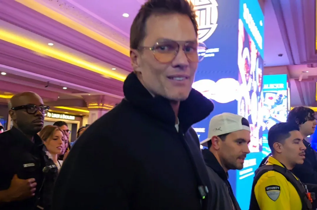 Tom Brady in sunglasses interacting with a fan in a chaotic hallway during a card shop launch in a Las Vegas casino.