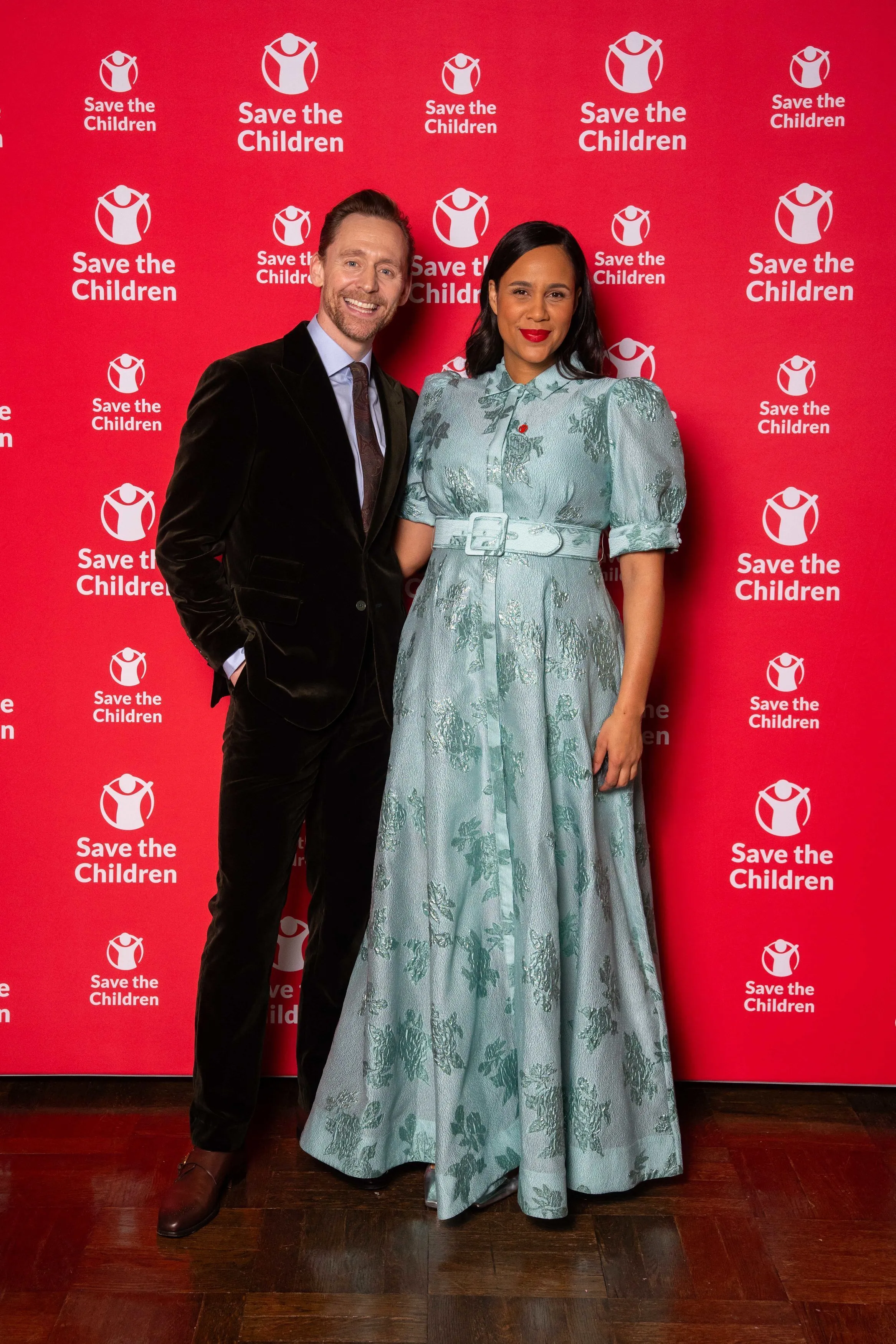 Tom Hiddleston and Zawe Ashton stand together against a red background with