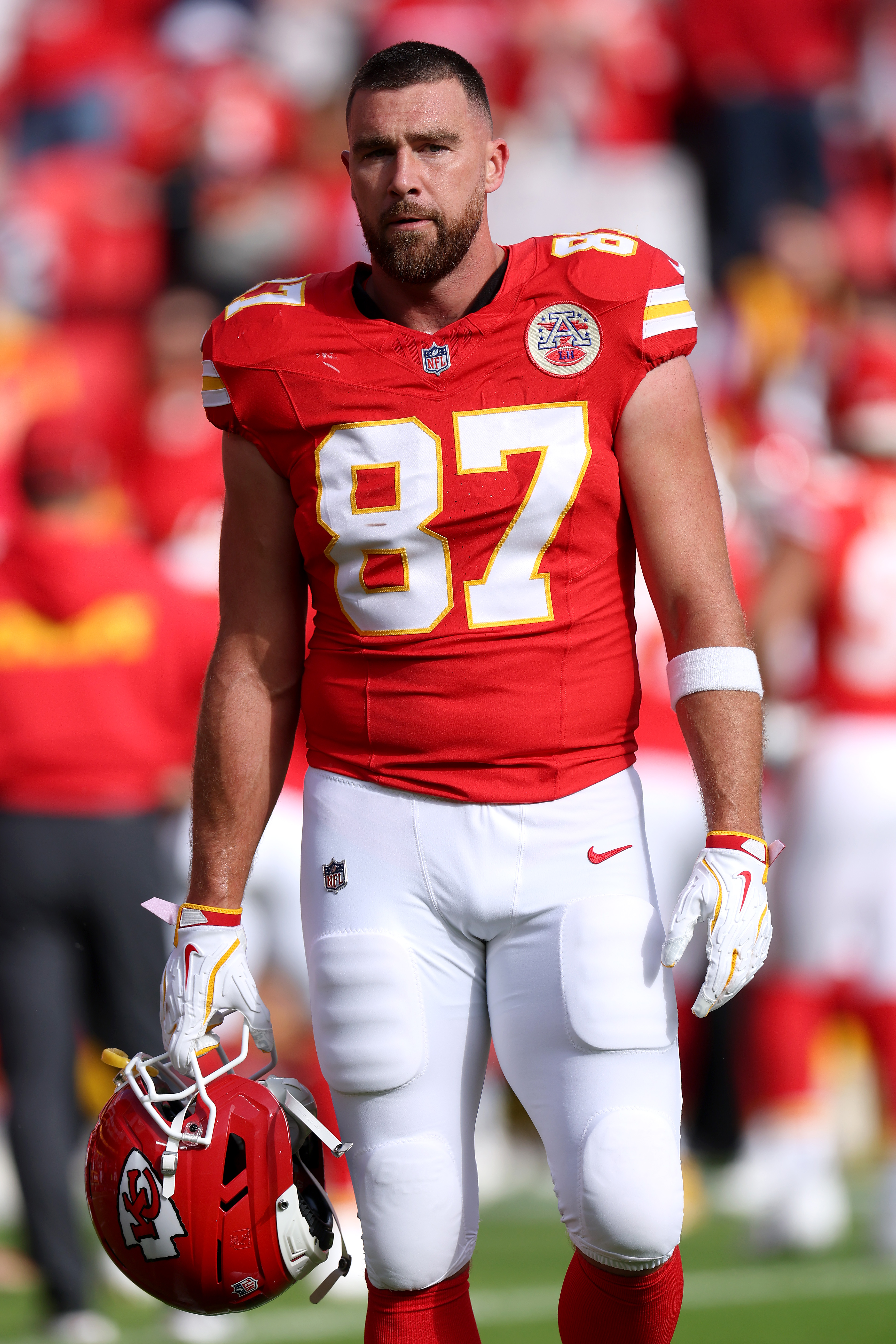 Travis Kelce in a red Kansas City Chiefs uniform with number 87, holding a red helmet.